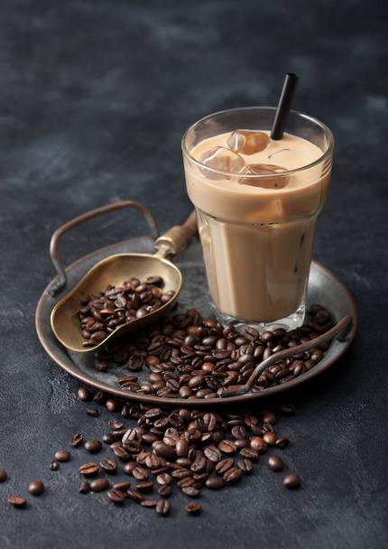 Glass of iced coffee drink with straw on tray with coffee beans and scoop on black background. Top view - Foto, Imagem