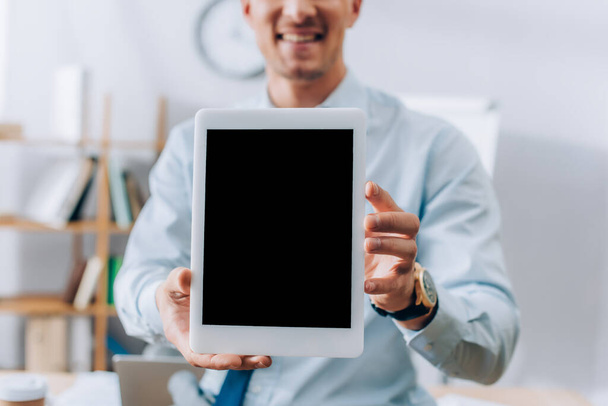 Cropped view of digital tablet with blank screen in hands of smiling businessman on blurred background  - Fotó, kép