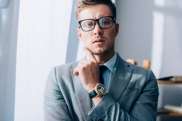 Businessman in eyeglasses and suit looking at camera in office  - Fotoğraf, Görsel