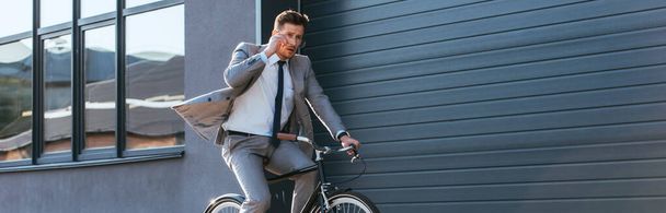 Young businessman in formal wear holding eyeglasses while cycling near building, banner  - Foto, Imagem