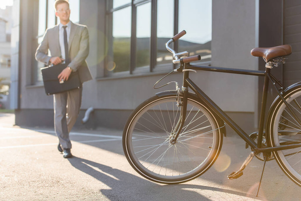Bicycle near walking businessman with briefcase on blurred background outdoors  - Foto, Imagen