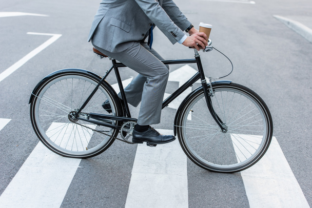 Cropped view of businessman holding takeaway coffee while cycling on crosswalk  - Fotografie, Obrázek