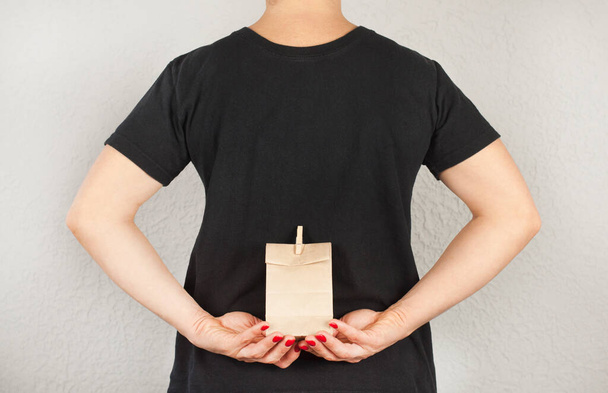 Μια γυναίκα με μπλουζάκι κρατάει μια χάρτινη σακούλα. Παρόντες - Φωτογραφία, εικόνα