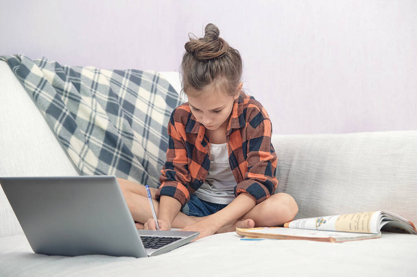 Child sits on the couch at home and does online lessons - Photo, image
