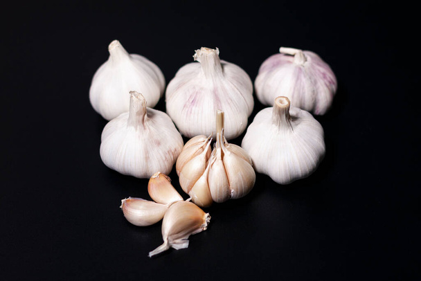 Young garlic heads are located on a dark surface. Near individual cloves of vegetable. - Φωτογραφία, εικόνα