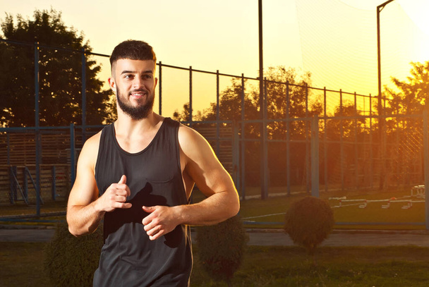 A man runs on the playground. Athlete on a sunset background. - Photo, Image