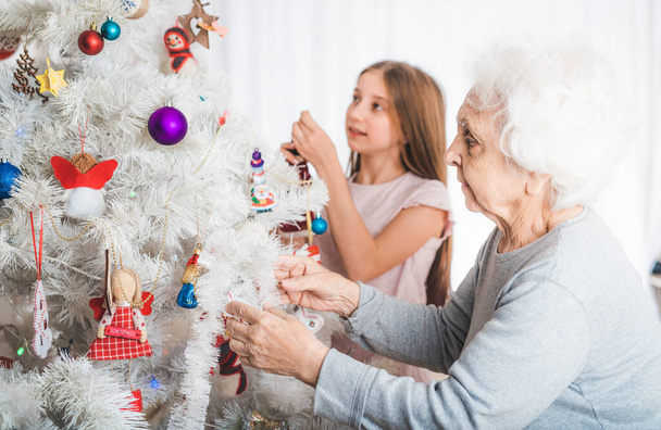 Granddaughter with grandma decorating christmas tree - 写真・画像