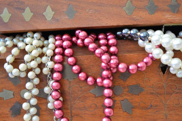 Gros plan de plusieurs colliers de perles sortant d'une boîte en bois avec des décorations indiennes - Photo, image