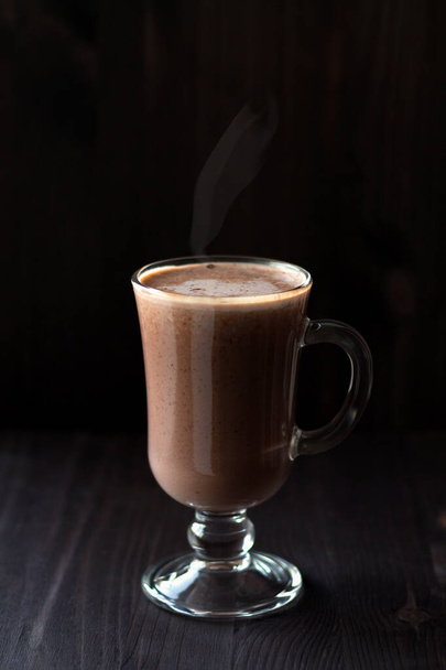 Bir fincan sıcak çikolata. Karanlık bir masada bir bardak kapuçino. İçkiler ahşap arka planda. Sıcak içecekler kış ve sonbahar. Dikey. Boşluğu kopyala - Fotoğraf, Görsel