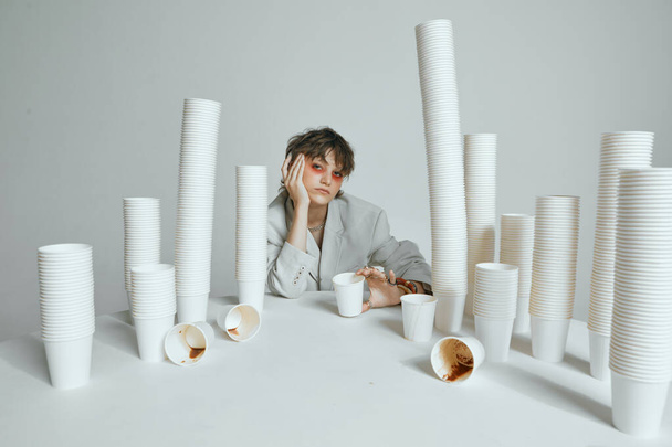 Tired girl with lots of paper cups for coffee on gray studio background - Fotó, kép