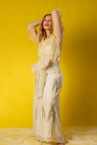 Mujer joven y bella vestida con falda y blusa vaporosa sobre fondo amarillo, en sesion fotografica en estudio - Фото, зображення