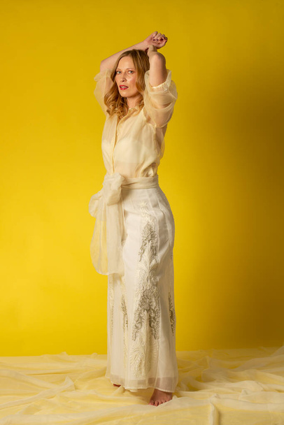 Mujer joven y bella vestda con falda y blusa vaposa sobore fondo amarillo, en sesion fotografica en estudio - 写真・画像