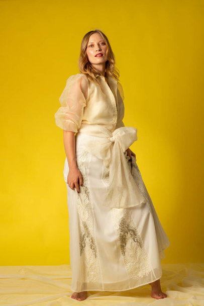 Mujer joven y bella vestida con falda y blusa vaporosa sobre fondo amarillo, en sesion fotografica en estudio - Foto, Bild