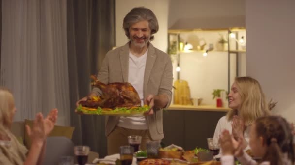 Sekwencja zdjęć dojrzałego mężczyzny przynoszącego pysznego pieczonego indyka i krojącego go dla swojej rodziny w Święto Dziękczynienia - Materiał filmowy, wideo