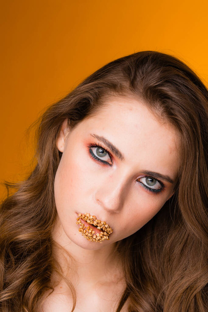 Creative makeup with buckwheat on the lips. The girl stands on an orange background. Pandemic food shortage concept - Foto, Imagem