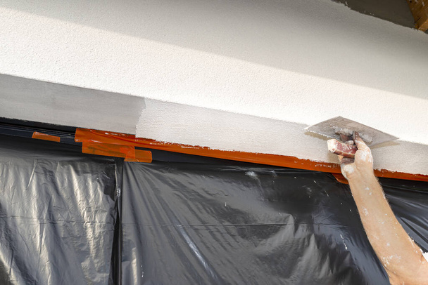 Een bouwvakker brengt een witte laag siliconen gips aan en vervaagt deze over de ruiten, het raam is beschermd met folie. - Foto, afbeelding