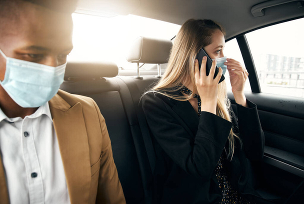 Business Couple Wearing Masks Using Laptop And Mobile Phone In Back Of Taxi During Health Pandemic - Photo, Image