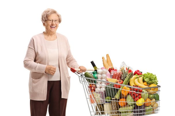 Elderly woman posing with a shopping cart isolated on white background - Foto, Imagem