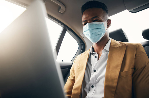 健康の流行の間のタクシーの背部のラップトップで働くマスクを身に着けている若いビジネスマン - 写真・画像