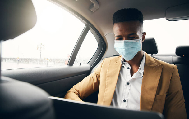 健康の流行の間のタクシーの背部のラップトップで働くマスクを身に着けている若いビジネスマン - 写真・画像