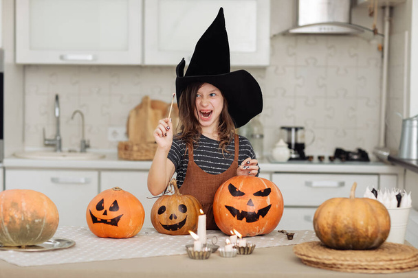 Fijne Halloween. Schattig klein meisje in heksenkostuum met gesneden pompoen. Gelukkige familie bereidt zich voor op Halloween. meisje steekt kaarsen aan. - Foto, afbeelding