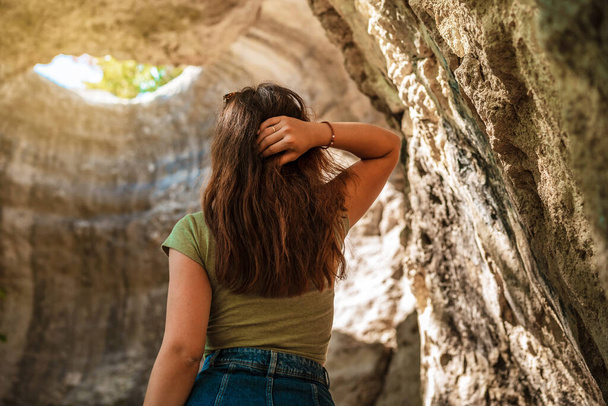 Zadní pohled na mladou ženu dobrodruh stojí v podzemní jeskyni s otvorem ven, Sluneční světlo přes jeskyni - Fotografie, Obrázek