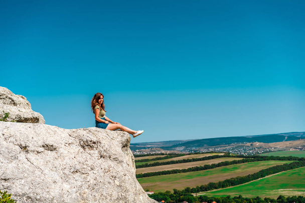 A young woman stands on a rock overlooking a green valley - Foto, Imagem