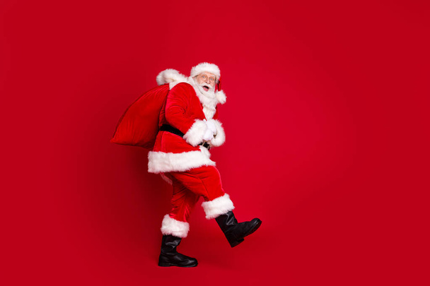 Photo portrait of amazed santa claus with open mouth carrying huge bag of gifts isolated on bright red colored background - Фото, зображення