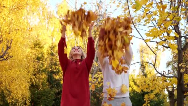Θετικοί άνδρες και γυναίκες ρίχνουν ξηρά κίτρινα φύλλα στο πάρκο - Πλάνα, βίντεο