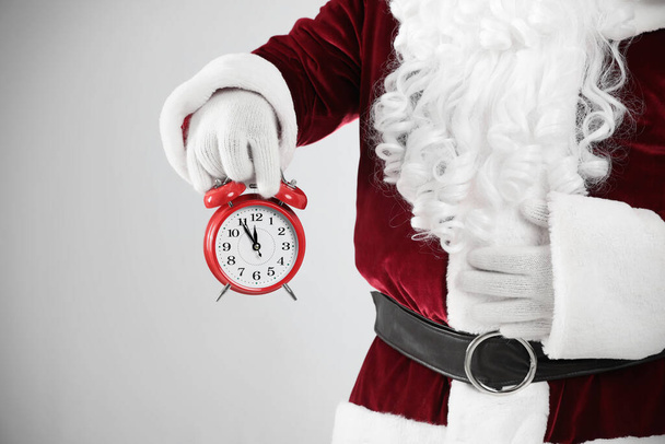 Santa Claus holding alarm clock on light grey background, closeup. Christmas countdown - Φωτογραφία, εικόνα