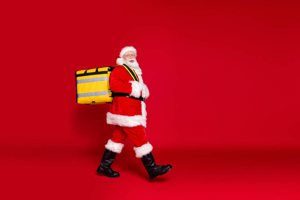 Full length body size profile side view of his he handsome cheery bearded Santa father carrying box festal delivery celebrate newyear isolated bright vivid shine vibrant red color background - Фото, изображение