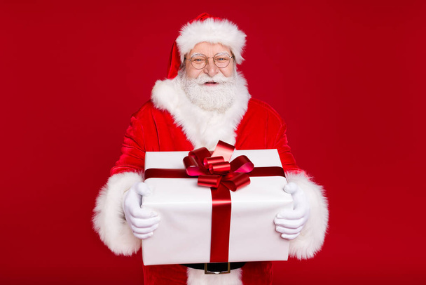 Muotokuva hänen hän mukava komea houkutteleva iloinen iloinen ylipainoinen parrakas Santa isä tilalla käsissä iso iso valkoinen lahjapaketti juhlia eristetty kirkas eloisa loistaa elinvoimainen punainen väri tausta - Valokuva, kuva