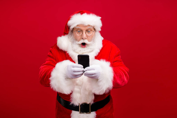 Portrét jeho pěkný atraktivní pohledný ohromený Santa pomocí gadget 5g rychlý rychlostní blog blogger procházení multimédií izolované přes světlé živé zářivá červená barva pozadí - Fotografie, Obrázek