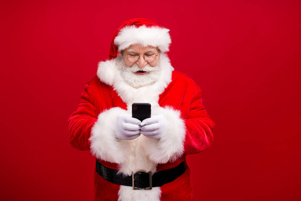 Portrét jeho pěkný atraktivní pohledný veselý veselý soustředěný Santa pomocí gadget 5g rychlé rychlosti blog blogger post komentář média izolované přes jasný živý lesk pulzující červené barvy pozadí - Fotografie, Obrázek