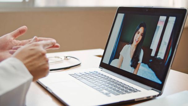 Lekarz online rozmowy wideo wyjaśnić leczenie, sprawdzenie objawów z azjatycką pacjentką łączącą się z domu, za pomocą laptopa w biurze szpitalnym. Telemedyczny, Covid-19 nowa koncepcja normalnej opieki zdrowotnej - Zdjęcie, obraz