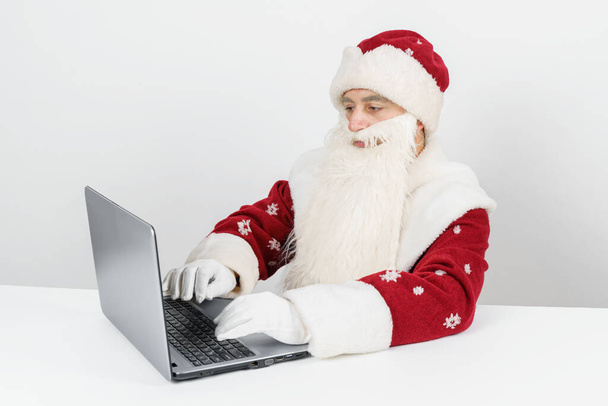 Christmas and New Year concept. Santa Claus sits at his desk and works at the computer. - Foto, Bild