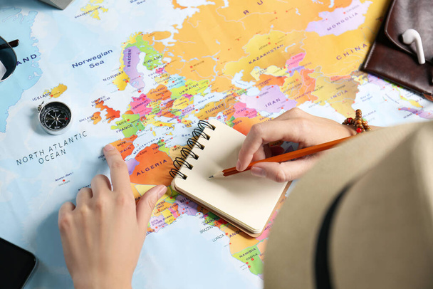Woman using world map to plan trip at wooden table, closeup - Photo, Image