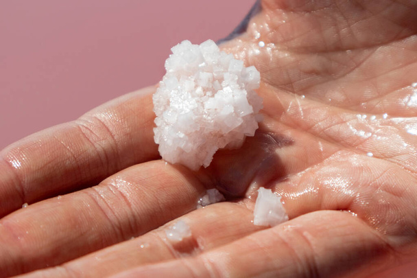 Hand houden roze witte zout vlok kristalvorming in de buurt van roze levendige meer wateroppervlak. Spa resort zonnige close-up op Syvash, Oekraïne - Foto, afbeelding