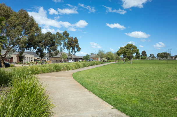 Een gebogen voetpad / loopbrug in een voorstedelijk park met enkele moderne Australische huizen / huizen in de verte. Achtergrond textuur van een lokaal park met grote gazon en open ruimte. Kopieer ruimte voor tekst - Foto, afbeelding
