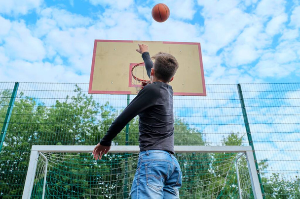 Teenager boy jumping with ball playing street basketball, back view - Photo, image