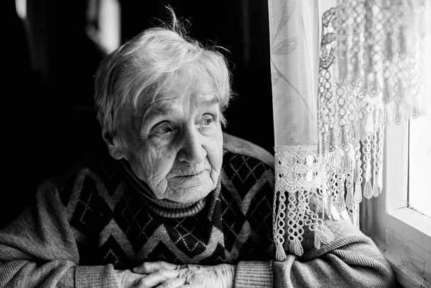 Une vieille femme regardant par la fenêtre. Photographie noir et blanc. - Photo, image