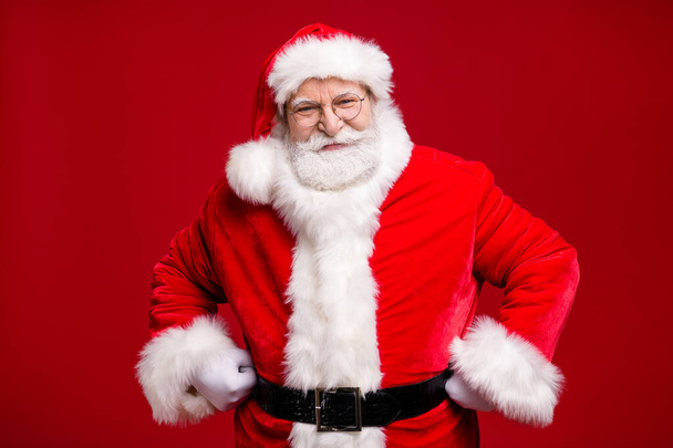 Photo of retired old man grey beard fists hips self-assured attend educate naughty kid play strict grandpa wear santa costume belt coat spectacles headwear isolated red color background - Foto, Imagen