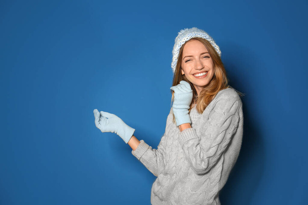 Happy young woman wearing warm sweater, knitted hat and mittens on blue background - Фото, зображення