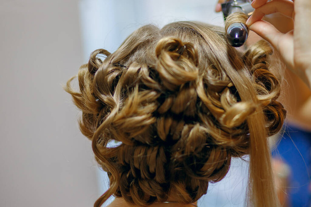 Curlers make curls on women's hair. Hairdresser services for the concept of evening and festive hairstyles. Close-up curls and curling iron that makes them - Fotografie, Obrázek