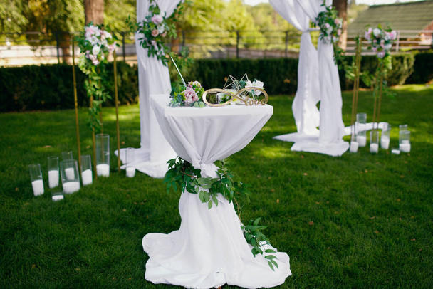 Εξωτερική γαμήλια τελετή για τη νύφη και το γαμπρό, διακοσμημένη με ένα τραπέζι με φρέσκα λουλούδια, ένα σύμβολο του απείρου και ένα γυάλινο κουτί κάτω από τα δαχτυλίδια. Ελεύθερος χώρος για κείμενο - Φωτογραφία, εικόνα