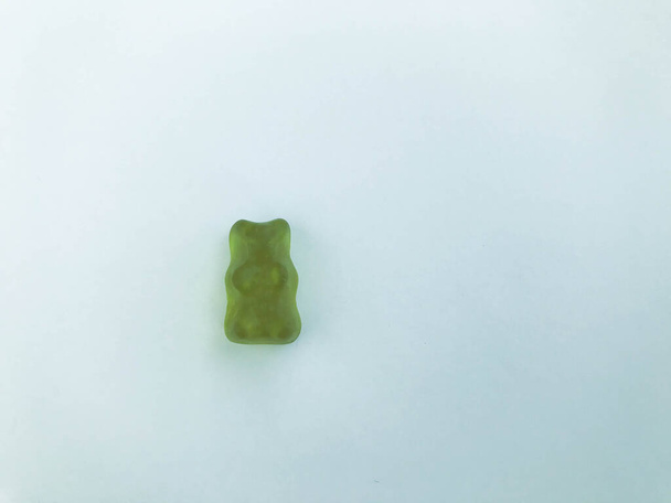 grüner, gallertartiger Bär auf mattweißem Hintergrund. Gummifigur in Form eines Tieres. Bonbons. süße appetitliche Figur. Kalorienreiches Dessert für Kinder und Erwachsene - Foto, Bild