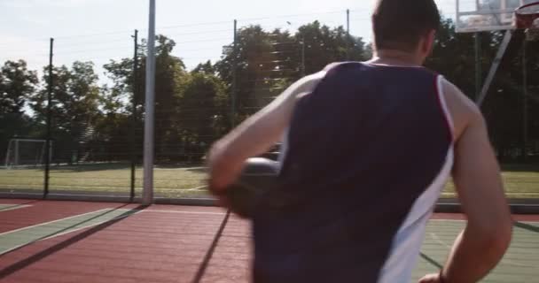 Fiatal férfi dobott labdát a karika, játszik egyedül kosárlabda pályán - Felvétel, videó