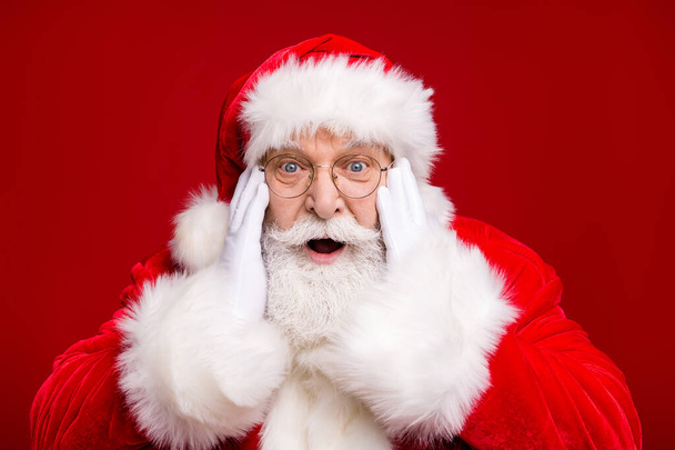 Photo of retired old man grey beard open mouth excited look hand cheekbone magical event deer start flying wear santa costume coat spectacles headwear isolated red color background - Fotoğraf, Görsel