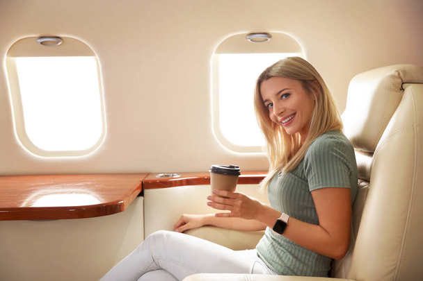 Beautiful woman with paper cup on plane. Air travel - Φωτογραφία, εικόνα