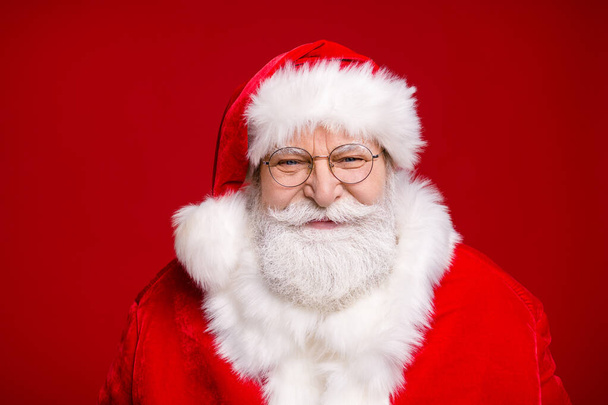 Photo of pensioner old man grey beard wait listen children sitting knee make wish smiling prepare show giftbox wear santa costume coat spectacles headwear isolated red color background - Фото, изображение